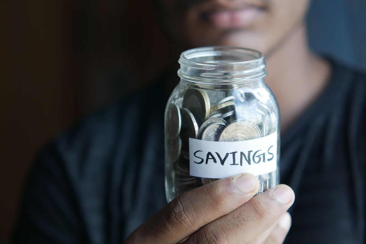सिक्कों से भरा Savings जार हाथ में पकड़े व्यक्ति — इमरजेंसी फंड कैसे बनाएं 2026